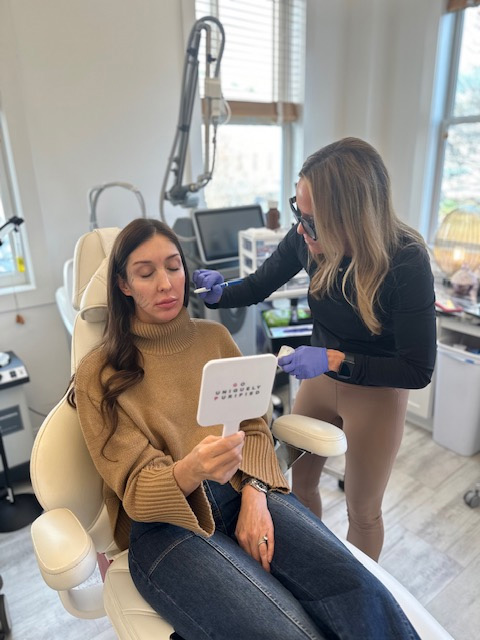 Woman sitting in a chair looking at mirror | United Medical And Aesthetics in Wilmington, NC